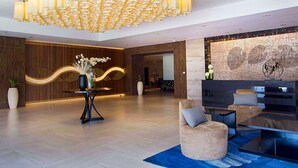 A modern lobby with a large chandelier, a reception desk, seating area, and a wall with a decorative design. - 8 Newtown Boulevard by HiveRooms (Lapu-Lapu)