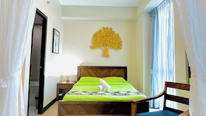 A bedroom with a bed, a chair, a nightstand, a wall art piece, and a door. - 8 Newtown Boulevard by HiveRooms (Lapu-Lapu)