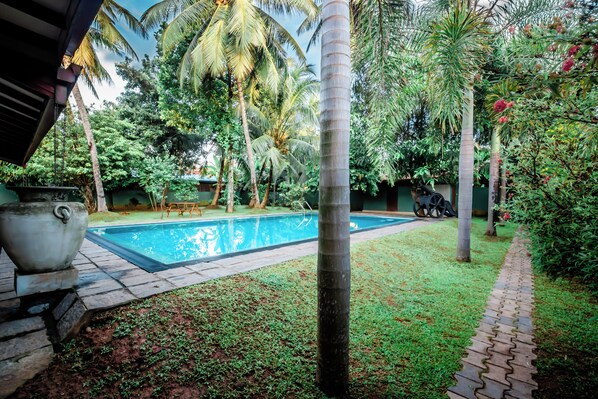 A pool area with a tiled deck, palm trees, and a grassy lawn. - Beru Villa (Beruwala)