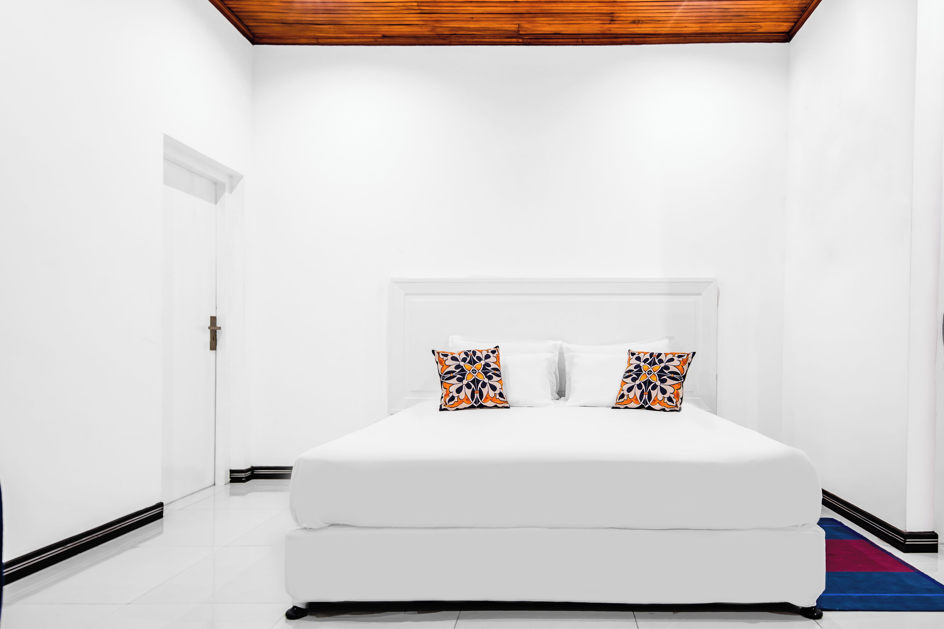 A bedroom with a white bed, two patterned pillows, a wooden ceiling, and a white door.