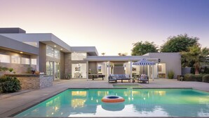 Ein modernes Haus mit Swimmingpool, Sitzgelegenheiten im Freien und einer überdachten Terrasse.