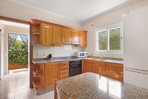 A kitchen with wooden cabinets, granite countertops, a microwave, an oven, and a refrigerator. - Villa Gioia (Llucmajor)
