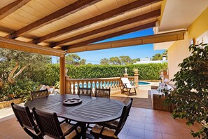 An outdoor patio with a round table and chairs, a pool, and a view of greenery. - Villa Gioia (Llucmajor)