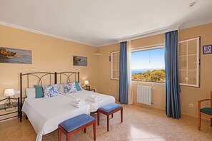 A bedroom with a large bed, two bedside tables with lamps, a view of the sea, and a window with curtains. - Villa Gioia (Llucmajor)