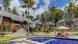 A pool area with lounge chairs and a covered seating area, surrounded by palm trees and a stone staircase leading to a building. - Ume Sari Nusa (Penida Island)