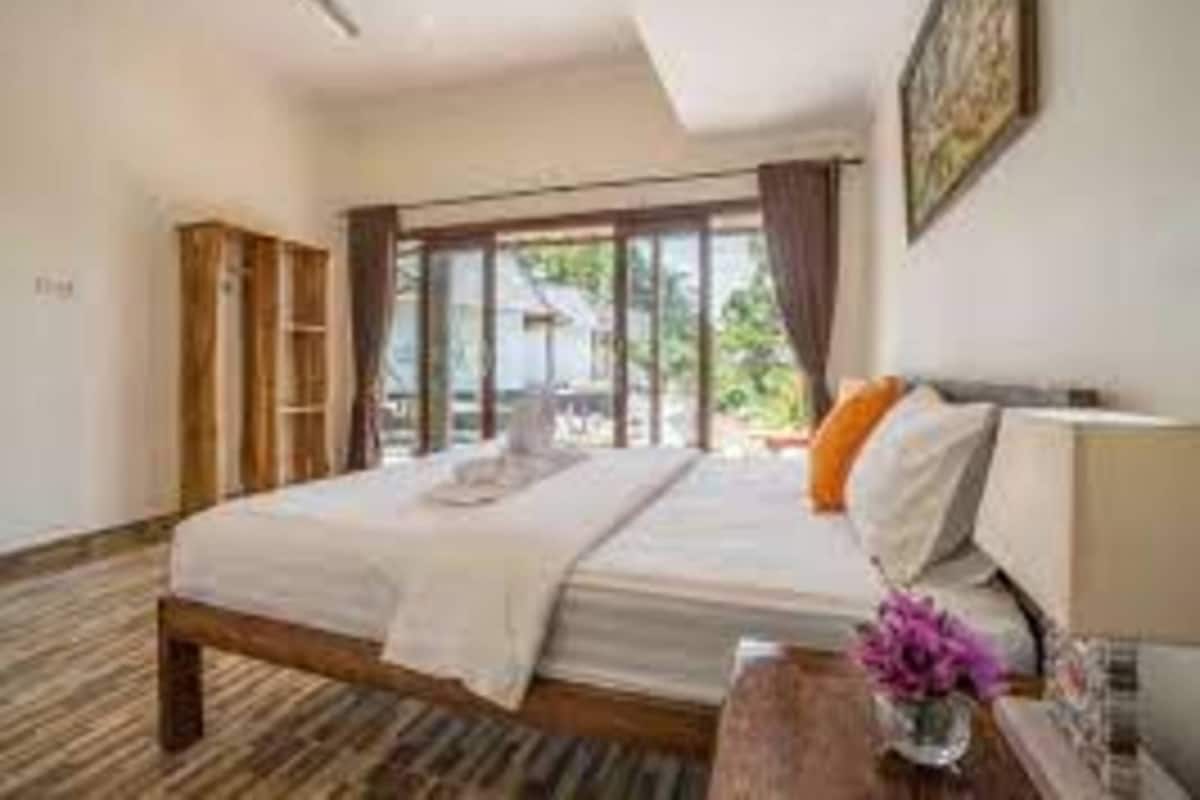 Ein Schlafzimmer mit einem Bett, einem Nachttisch, einem Fenster mit Vorhängen und einem Deckenventilator.