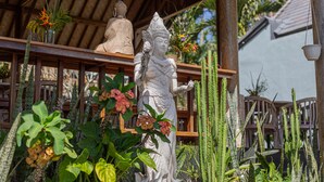 A statue of a figure in traditional attire, surrounded by various plants and a wooden structure. - Ume Sari Nusa (Penida Island)