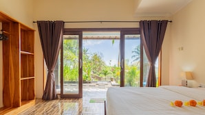 A hotel room with a bed, a wooden wardrobe, and a sliding glass door leading to a balcony with a view of greenery. - Ume Sari Nusa (Penida Island)