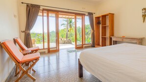 A bedroom with a bed, a wooden wardrobe, a seating area with chairs, and a view through the glass doors. - Ume Sari Nusa (Penida Island)