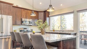 A modern kitchen with dark wood cabinets, stainless steel appliances, and a large island with bar stools. - 2 Decks, Views, Firepit | Cozy Modern & Relaxing Home | Blue Spruce by AvantStay (Lake Arrowhead)