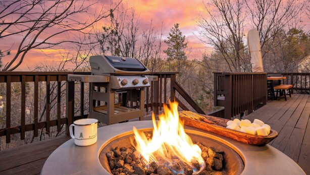 A barbecue grill with a fire, a bowl of marshmallows, and a mug on a deck. - 2 Decks, Views, Firepit | Cozy Modern & Relaxing Home | Blue Spruce by AvantStay (Lake Arrowhead)
