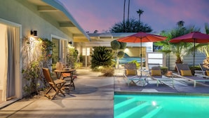 A pool area with lounge chairs and umbrellas, surrounded by plants and a building facade. - Retro Oasis w/ Pool, Ping Pong, & Large Yard | Lloyd by AvantStay Permit#3779 (Palm Springs)
