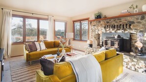 A living room with a yellow sofa, a stone fireplace, and large windows. - 3.5-Acre 5BDR Rereat w/ Views, Pool + Hot Tub, Fire Pit | Gable by AvantStay (Santa Rosa)
