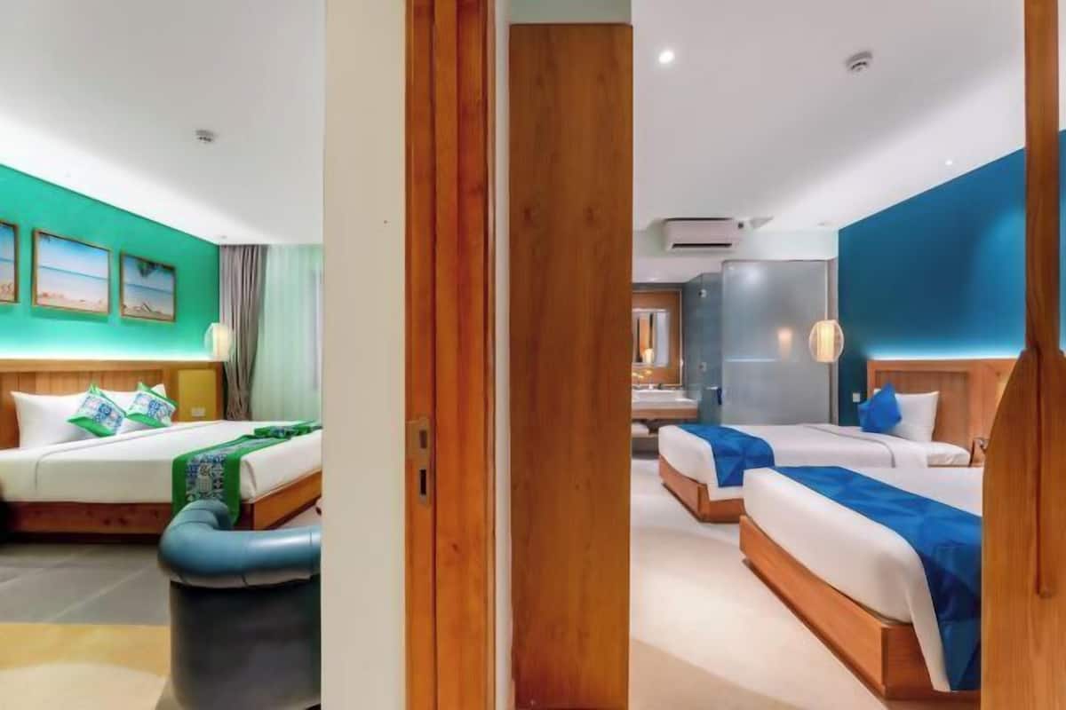 Een hotelkamer met twee bedden, een houten deur en uitzicht op de gang.