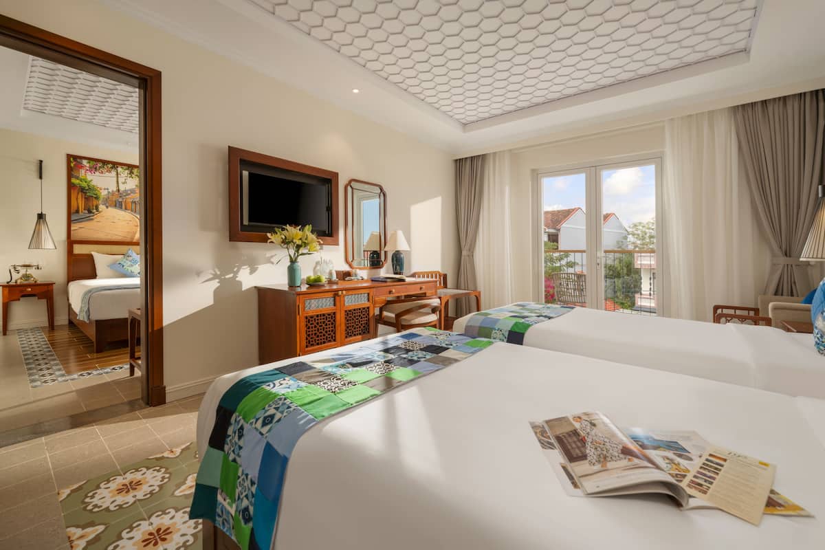 Een hotelkamer met twee bedden, een bureau, een stoel, een televisie en een balkon met gordijnen.