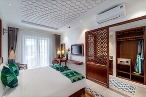 Une chambre d’hôtel avec un grand lit, une télévision, un bureau avec une lampe et une armoire dont la porte est ornée d’un motif.