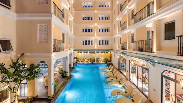 A multi-story hotel interior with a central swimming pool, multiple balconies, and indoor seating areas. - Amina Lantana Hoi An Hotel & Spa (Da Nang)