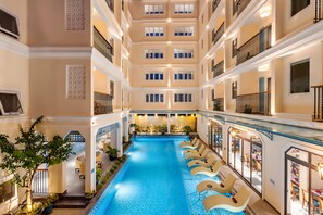 Innenansicht eines Mehrstöckigen Hotels mit einem zentralen Schwimmbecken, mehreren Balkonen und Sitzbereichen.