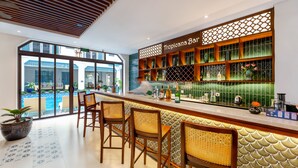 A bar area with a tropical theme, including a sign reading "Tropicana Bar," a variety of bottles, and a view of the pool outside. - Amina Lantana Hoi An Hotel & Spa (Da Nang)
