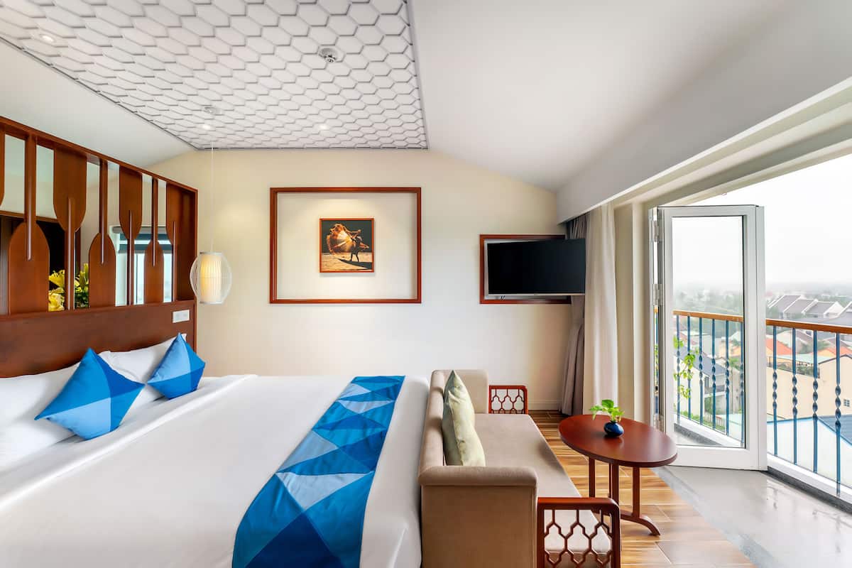 Hotelkamer met een groot bed, een bank, een kleine tafel, een televisie en een balkon met uitzicht.
