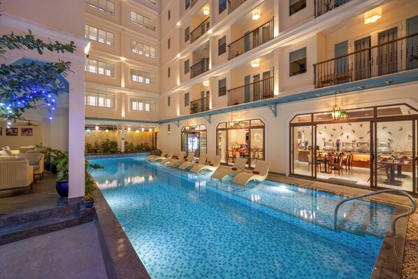 Un hôtel à plusieurs étages doté d’une piscine, de chaises longues et d’un restaurant/bar.