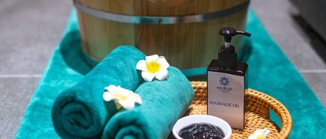 A spa setting with wooden tubs, towels, and massage oil on a tray.