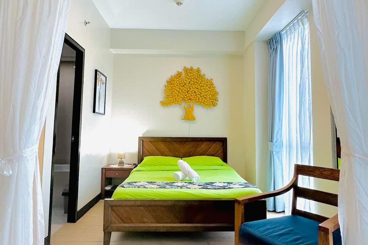 A bedroom with a bed, a chair, a nightstand, a wall art piece, and a door.
