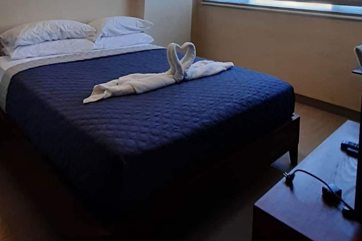 A hotel room with a bed, a desk, and a window with blinds.