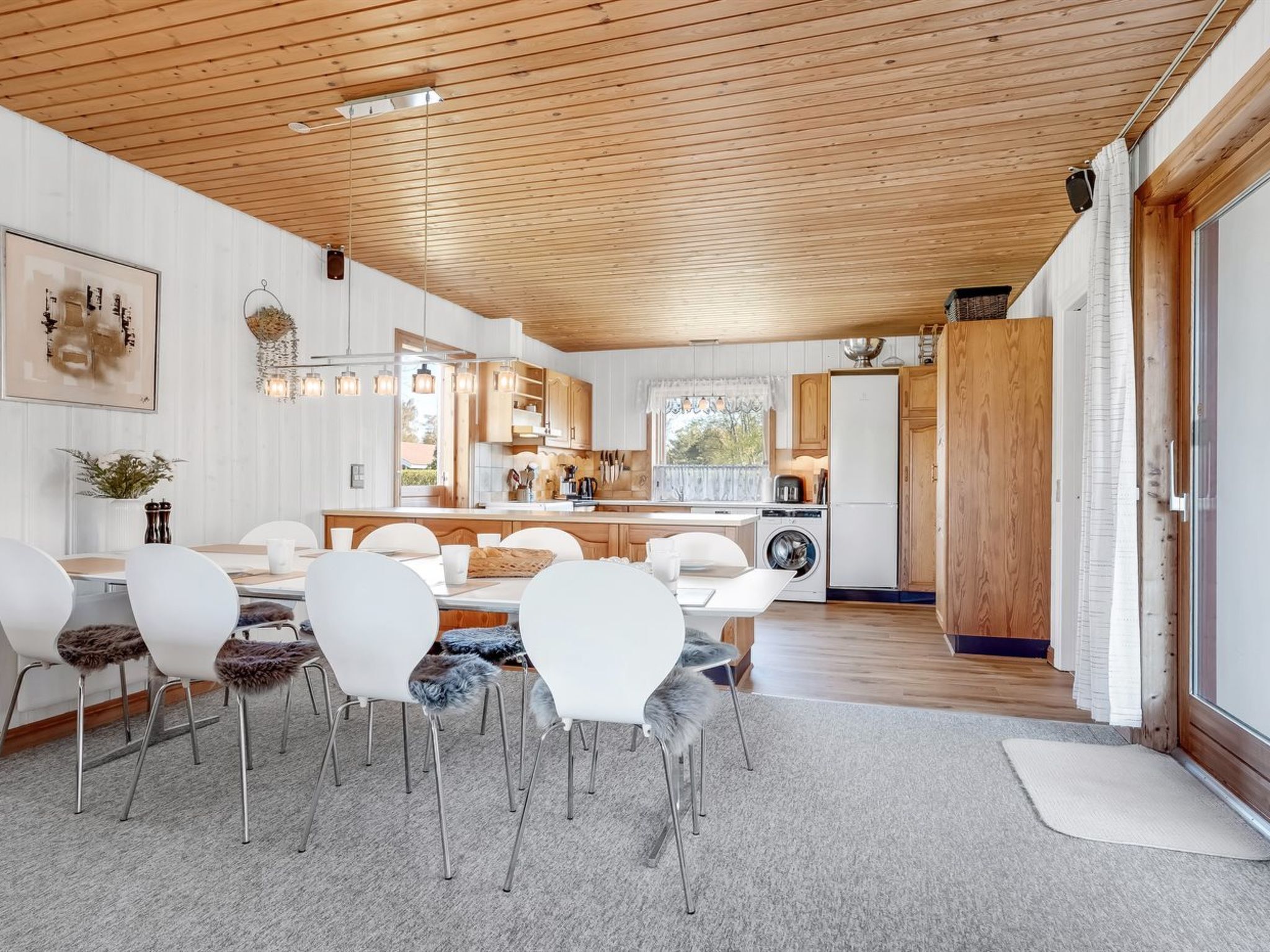 Ett modernt kök med träskåp, en köksö och en matplats med vita stolar och en matta.