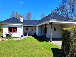 Ein zweistöckiges Haus mit überdachter Terrasse, Essbereich und gepflegtem Rasen.