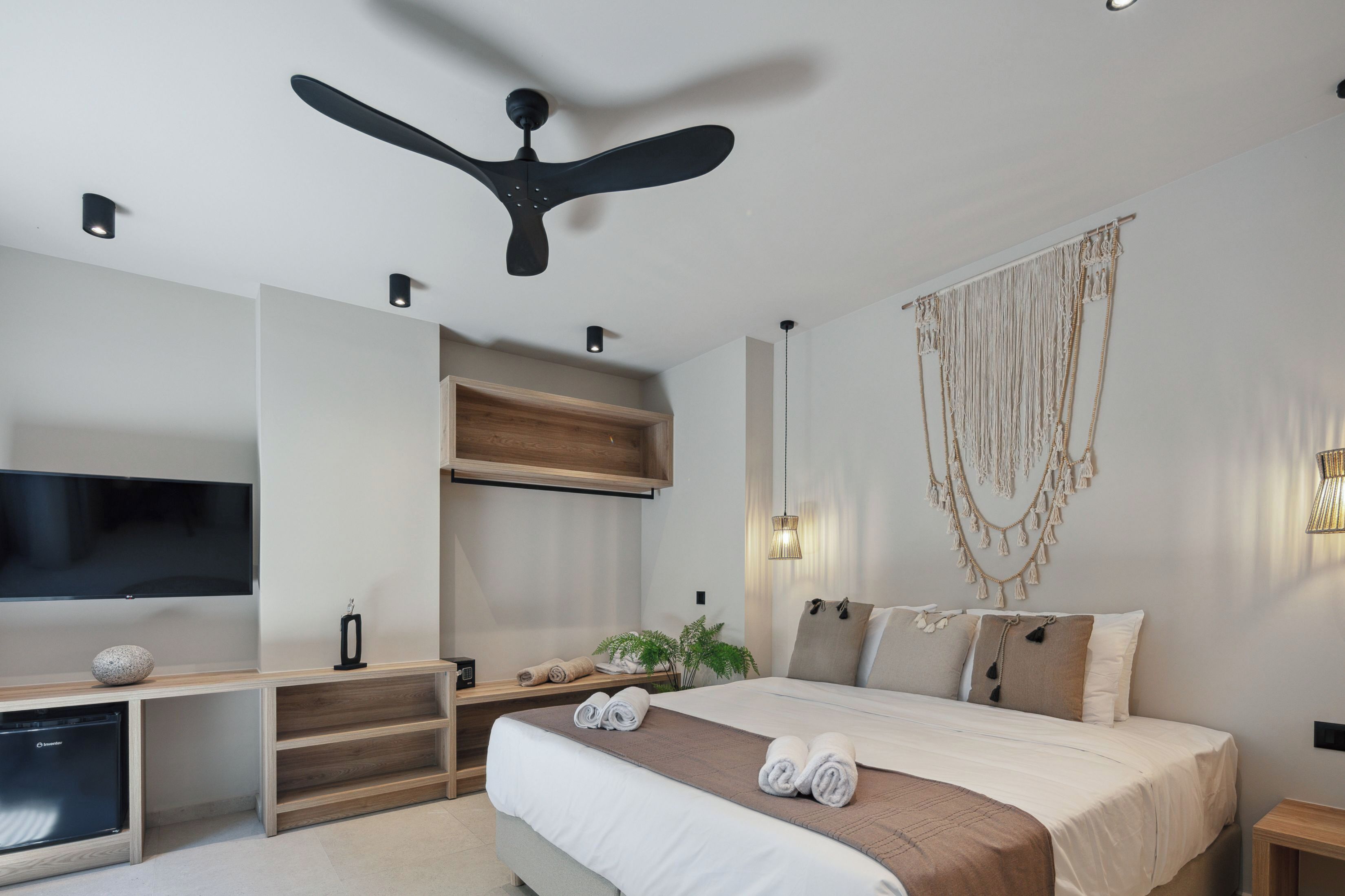 Une chambre moderne équipée d’un lit, d’un téléviseur à écran plat, d’un ventilateur de plafond et d’une étagère en bois.