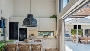 A modern kitchen with a dining area, featuring a large island, built-in appliances, and a view of the outdoors. - Luxury Villa with Sea Views, Fire Pit & near beach (Rethymno)