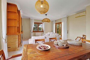 A dining area with a wooden table, white chairs, a white sofa, and a large woven pendant light. - Villa Santa Maria (Santa Maria del Camí)