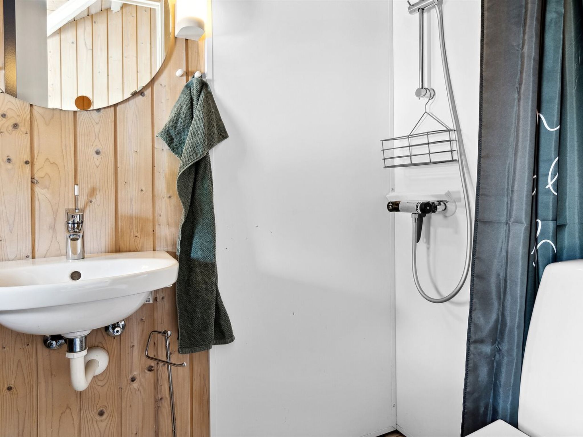 A bathroom with a wooden panel wall, a white sink, a towel, and a shower with a metal rack.