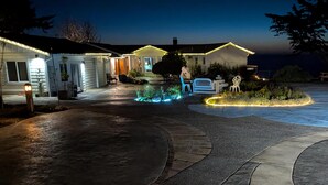 Una propietat residencial amb un camí d'accés que condueix a una casa, zona d'estar a l'aire lliure i il·luminació decorativa.