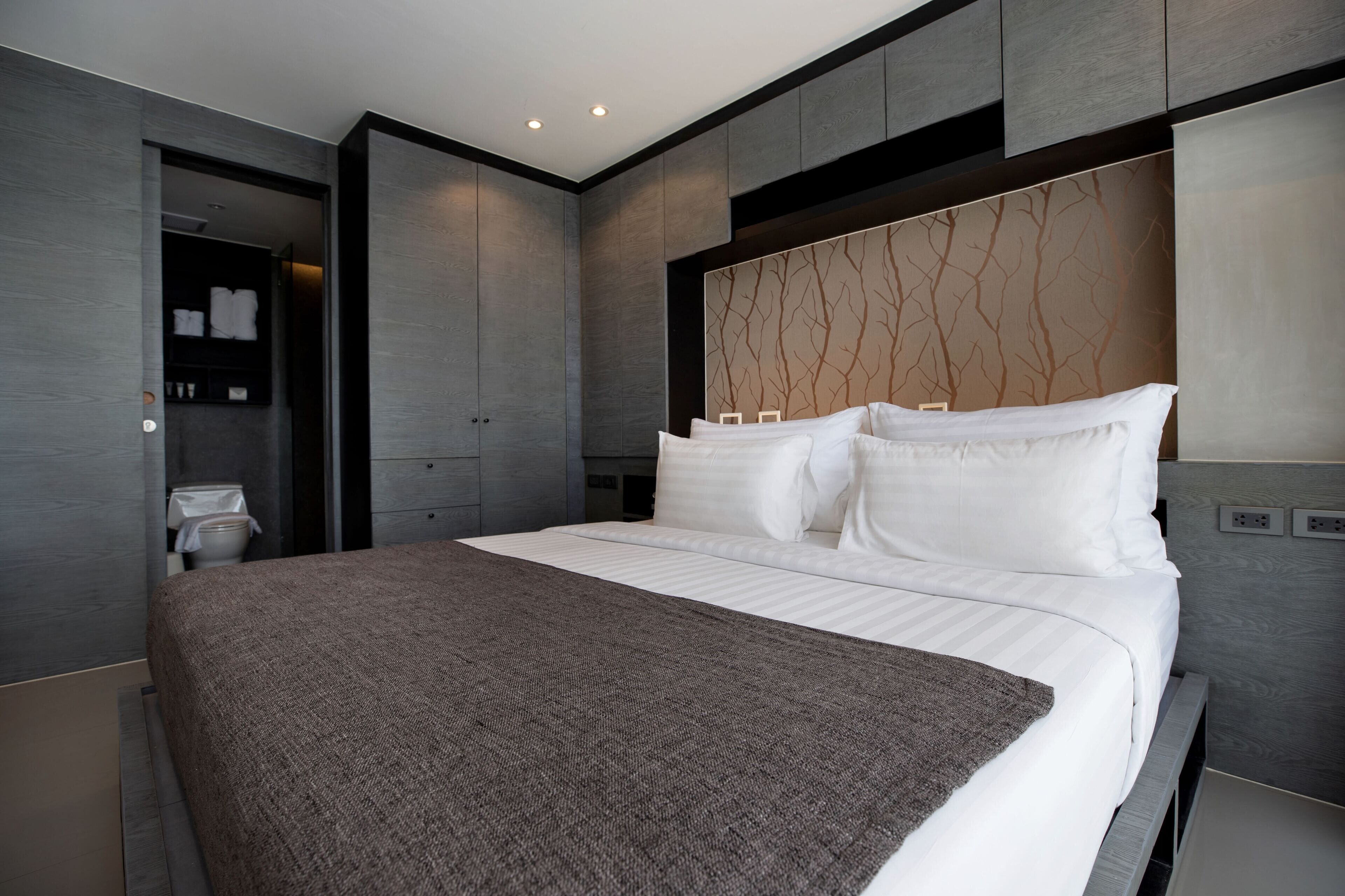 Une chambre moderne avec un grand lit, une armoire intégrée et une salle de bain visible à travers une porte ouverte.