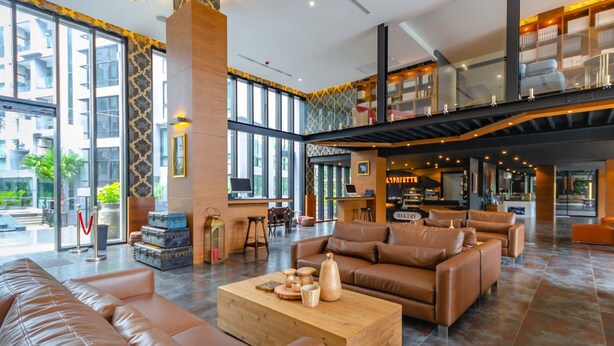 A spacious lobby with leather sofas, a wooden coffee table, and a bakery counter.
