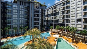 A modern hotel with multiple floors, a rooftop pool, and palm trees.