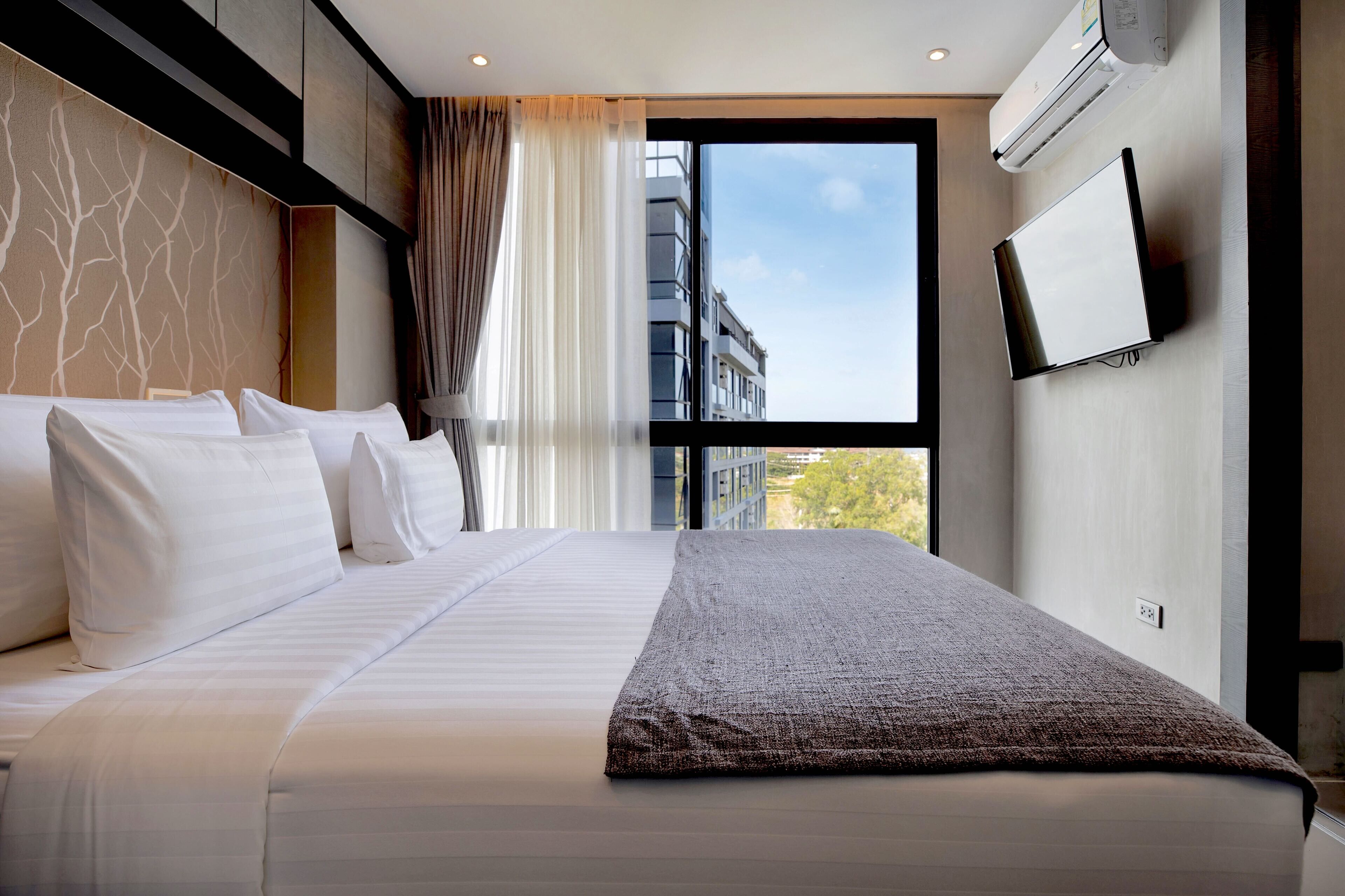Een hotelkamer met een groot bed, een aan de muur bevestigde televisie en een raam met uitzicht op gebouwen.
