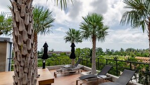 A rooftop terrace with lounge chairs, umbrellas, and a view of the landscape.