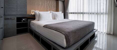A modern bedroom with a large bed, built-in storage, and a large window with sheer curtains.