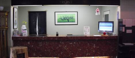 A reception desk with a marble counter, a framed picture of a tree, a computer monitor, and a sign with pricing information.