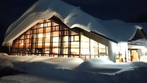 Un bâtiment moderne doté de grandes fenêtres et d’un toit incurvé original, entouré de neige.