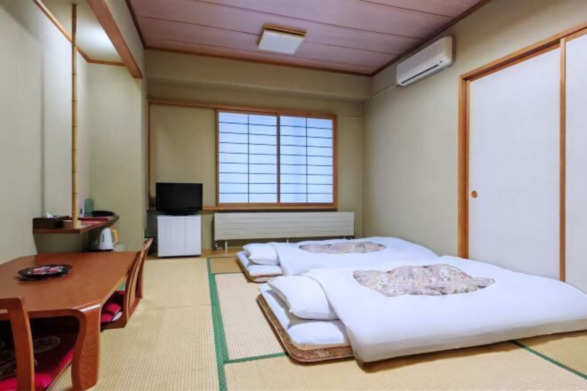 A traditional Japanese-style room with tatami flooring, a futon bed, a television, and a sliding door.