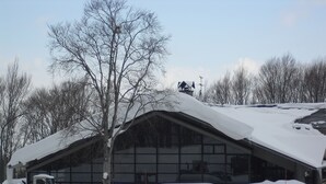 Un bâtiment doté d’un toit en pente recouvert de neige, entouré de véhicules garés.
