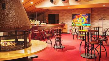 Un restaurant amb una xemenea central, diverses taules i cadires, zona de bar i un mural colorit a la paret.