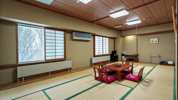 A traditional Japanese room with tatami flooring, a low wooden table with cushions, sliding doors, and a ceiling fan.