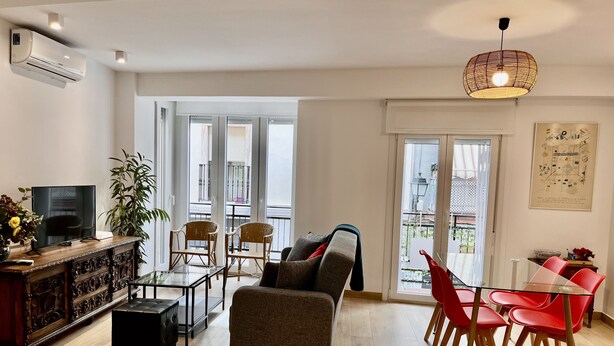 Un salon moderne avec un canapé, des fauteuils rouges, un téléviseur et un balcon offrant une vue agréable.