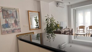 Une cuisine moderne avec un plan de travail noir, des armoires blanches et un grand miroir. Deux unités de climatisation sont fixées au mur, et une plante en pot est posée sur le plan de travail.