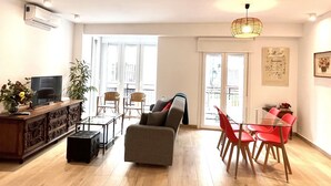 Un salon comprenant un téléviseur, un canapé, une table à manger, des chaises et un balcon doté d’une balustrade.